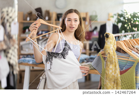 Positive young woman choosing something for summer in clothing store Positive young woman choosing something for summer in clothing store 142467264