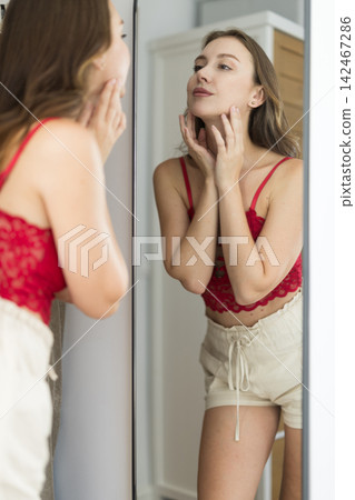 Adult woman looking into mirror in bedroom 142467286