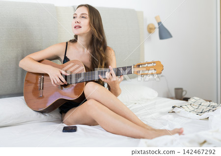 Pretty woman in lingerie sits on the bed and plays guitar Pretty woman in lingerie sits on the bed and plays guitar 142467292