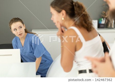 Woman stands near the reception of the dentistry and communicates with the administrator Woman stands near the reception of the dentistry and communicates with the administrator 142467362
