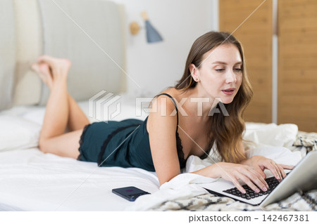 Woman in pajamas on bed with laptop Woman in pajamas on bed with laptop 142467381