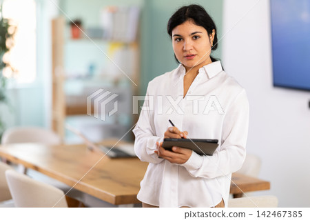 Portrait of friendly young woman with tablet in office or training room. Portrait of friendly young woman with tablet in office or training room. 142467385