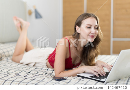 Woman in pajamas on bed with laptop 142467410