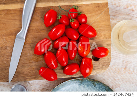 Pile of red cherry plum tomatoes on wooden cutting board Pile of red cherry plum tomatoes on wooden cutting board 142467424