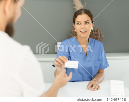 administrator gives man a business card of a dental clinic 142467428