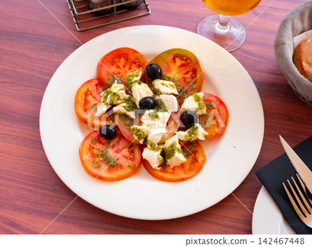 Appetizing salad of fresh ripe tomatoes with green pesto sauce and decorated with black olives. Italian cuisine Appetizing salad of fresh ripe tomatoes with green pesto sauce and decorated with black olives. Italian cuisine 142467448