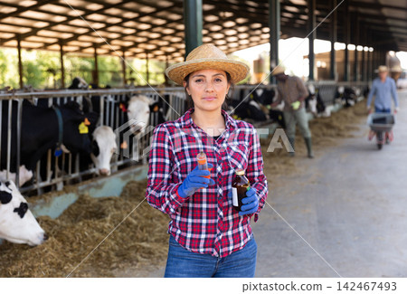 Female farmer standing near stall with cows with syringe Female farmer standing near stall with cows with syringe 142467493