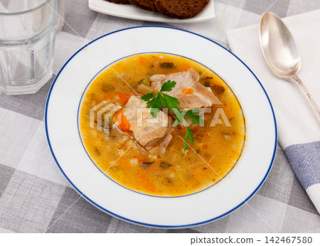 Pickle soup with pearl barley, potatoes, onions, carrots and parsley. Rassolnik in a white plate on a marble background. Traditional dish of Russian cuisine Pickle soup with pearl barley, potatoes, onions, carrots and parsley. Rassolnik in a white plate on a marble background. Traditional dish of Russian cuisine 142467580