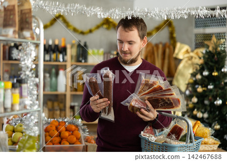 Young man choosing jamon and cured sausages for Christmas celebration in store Young man choosing jamon and cured sausages for Christmas celebration in store 142467688