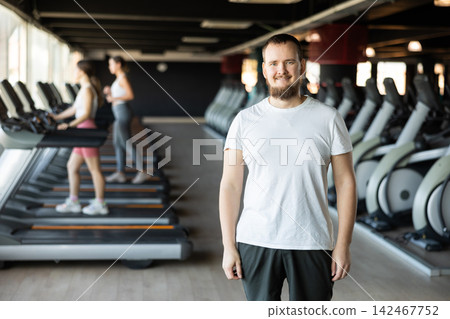 Young guy trainer in sportswear poses in middle of fitness center gym. Young guy trainer in sportswear poses in middle of fitness center gym. 142467752
