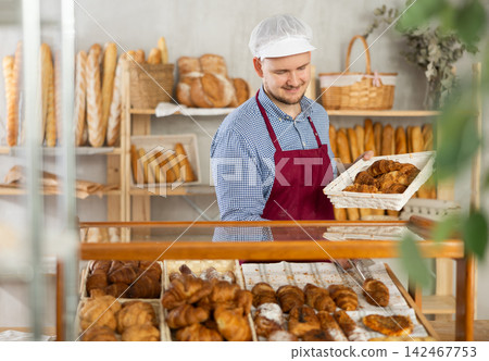 Selling fresh croissants in bakery - Baker places hot croissants on display Selling fresh croissants in bakery - Baker places hot croissants on display 142467753