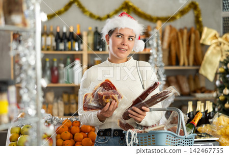 Female customer with a cart of groceries buys dried sausage and ham in supermarket - - prepares to celebrate Christmas Female customer with a cart of groceries buys dried sausage and ham in supermarket - - prepares to celebrate Christmas 142467755