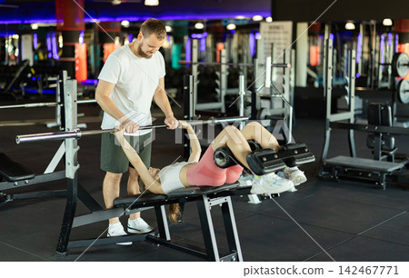 Girl does barbell exercises, and asks guy friend to insure her during exercises. Girl does barbell exercises, and asks guy friend to insure her during exercises. 142467771