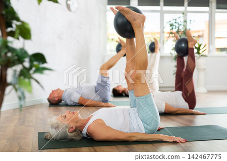 Mature woman doing exercises with pilates ball during group training at gym indoor 142467775