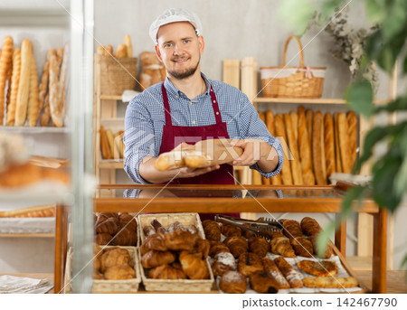 Bakery worker places fresh baguette in paper bag Bakery worker places fresh baguette in paper bag 142467790