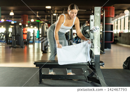 Girl lays white towel on bench, covers simulator for individual training. Girl lays white towel on bench, covers simulator for individual training. 142467793