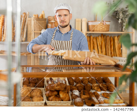 Man seller puts baguettes in paper bag for buyer, packs goods. 142467796