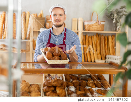 Selling fresh croissants in bakery - Baker places hot croissants on display 142467802