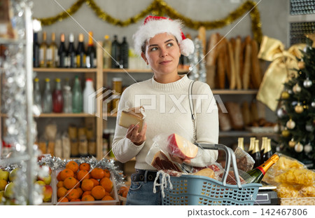 Female customer in Santa hat choosing cheese in festively decorated store Female customer in Santa hat choosing cheese in festively decorated store 142467806