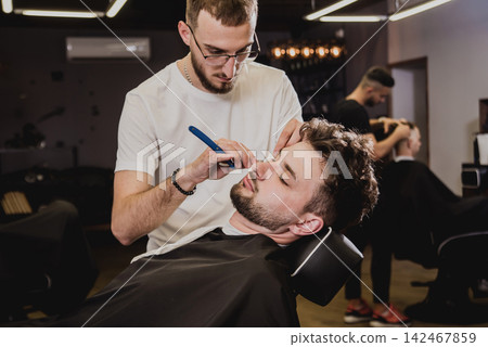 Young man with trendy haircut at barber shop. Barber does the hairstyle and beard trim. Young man with trendy haircut at barber shop. Barber does the hairstyle and beard trim. 142467859