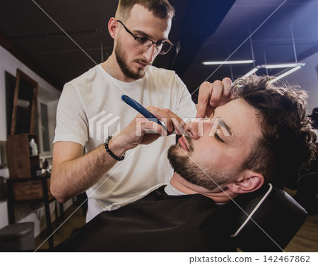 Young man with trendy haircut at barber shop. Barber does the hairstyle and beard trim. Young man with trendy haircut at barber shop. Barber does the hairstyle and beard trim. 142467862