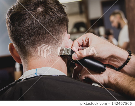 Young man with trendy haircut at barber shop. Barber does the hairstyle and beard trim. Young man with trendy haircut at barber shop. Barber does the hairstyle and beard trim. 142467866
