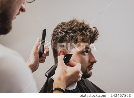 Young man with trendy haircut at barber shop. Barber does the hairstyle and beard trim. Young man with trendy haircut at barber shop. Barber does the hairstyle and beard trim. 142467868