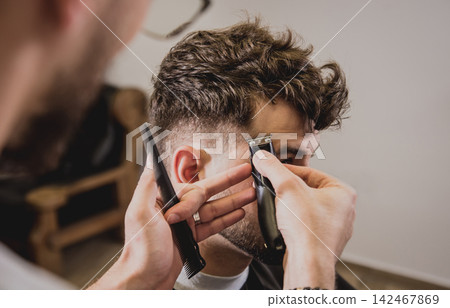 Young man with trendy haircut at barber shop. Barber does the hairstyle and beard trim. Young man with trendy haircut at barber shop. Barber does the hairstyle and beard trim. 142467869