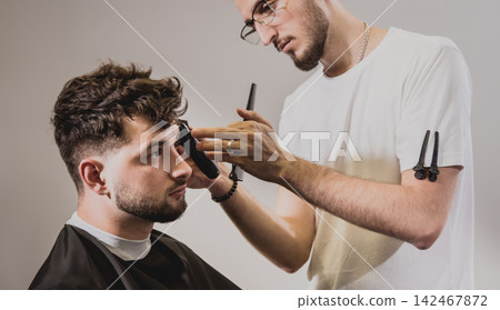 Young man with trendy haircut at barber shop. Barber does the hairstyle and beard trim. Young man with trendy haircut at barber shop. Barber does the hairstyle and beard trim. 142467872