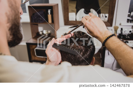 Young man with trendy haircut at barber shop. Barber does the hairstyle and beard trim. Young man with trendy haircut at barber shop. Barber does the hairstyle and beard trim. 142467878