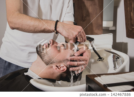 Young man with trendy haircut at barber shop. Barber washes customer head. Young man with trendy haircut at barber shop. Barber washes customer head. 142467886