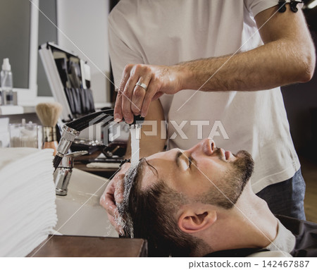 Young man with trendy haircut at barber shop. Barber washes customer head. Young man with trendy haircut at barber shop. Barber washes customer head. 142467887