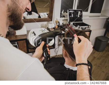 Young man with trendy haircut at barber shop. Barber does the hairstyle and beard trim. Young man with trendy haircut at barber shop. Barber does the hairstyle and beard trim. 142467888