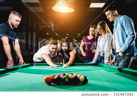 Group of young cheerful friends playing billiards. Group of young cheerful friends playing billiards. 142467891