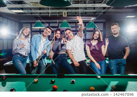 Group of young cheerful friends playing billiards. Group of young cheerful friends playing billiards. 142467896