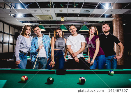 Group of young cheerful friends playing billiards. Group of young cheerful friends playing billiards. 142467897
