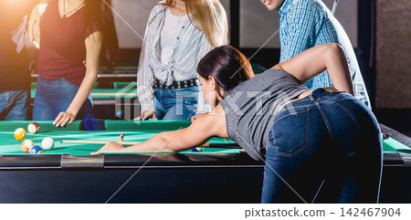 Young woman playing in billiard. Posing near the table with a cue in her hands Young woman playing in billiard. Posing near the table with a cue in her hands 142467904