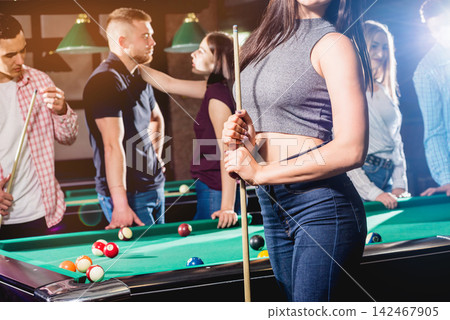 Young woman playing in billiard. Posing near the table with a cue in her hands Young woman playing in billiard. Posing near the table with a cue in her hands 142467905