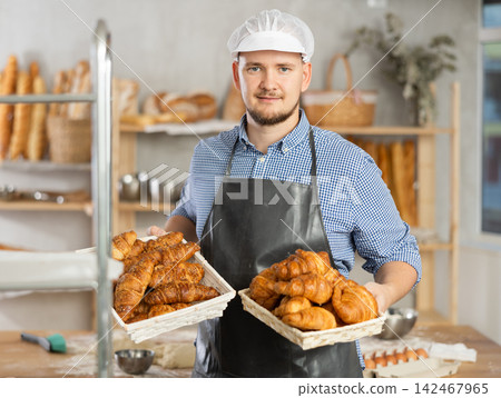 Male baker holds basket with finished products, shows many different croissants Male baker holds basket with finished products, shows many different croissants 142467965