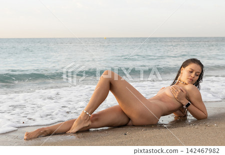 Erotic picture of naked woman sitting on sandy beach at sunset 142467982
