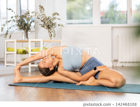 Lover of active lifestyle on yoga mat perform doing Parivritta Janu Shirshasana in gym Lover of active lifestyle on yoga mat perform doing Parivritta Janu Shirshasana in gym 142468108