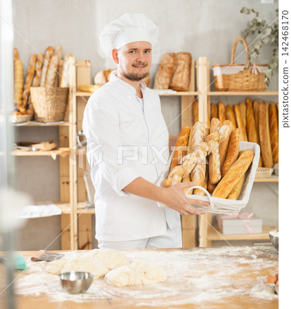 Male baker holds basket with finished products, shows many different baguettes Male baker holds basket with finished products, shows many different baguettes 142468170