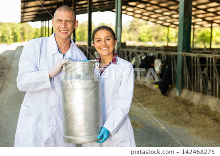 Smiling farmers holding large metallic milk can Smiling farmers holding large metallic milk can 142468275