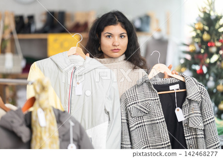 Latina chooses coats and jackets against the background of a Christmas tree Latina chooses coats and jackets against the background of a Christmas tree 142468277