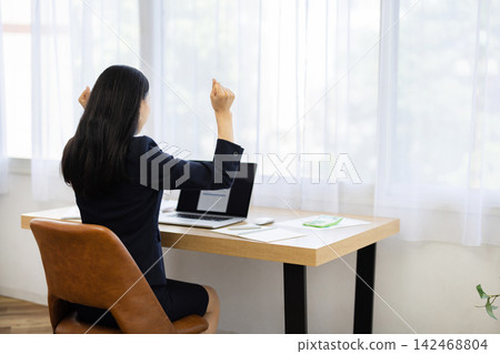 The back view of a young Japanese businesswoman, who is sitting at a desk by the window, looking at her computer and making a triumphant gesture. The back view of a young Japanese businesswoman, who is sitting at a desk by the window, looking at her computer and making a triumphant gesture. 142468804