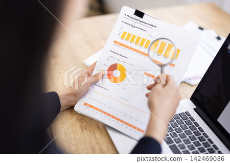 A close-up of a businesswoman's hands as she holds a magnifying glass over documents. A close-up of a businesswoman's hands as she holds a magnifying glass over documents. 142469086