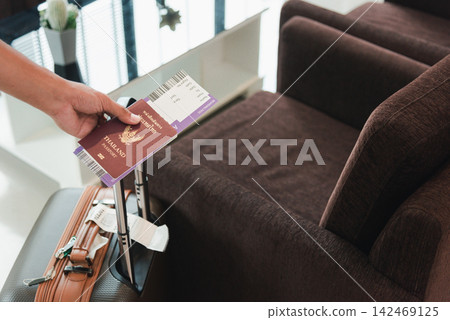 Close up hands the man going to flight with suitcase holding Thailand passport and airline ticket on baggage luggage Close up hands the man going to flight with suitcase holding Thailand passport and airline ticket on baggage luggage 142469125
