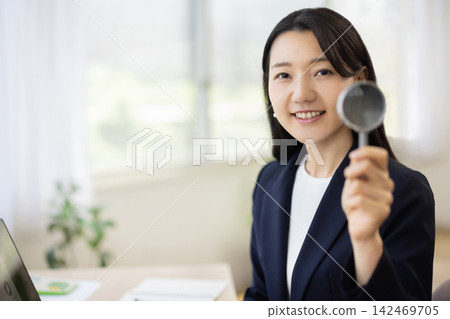 一位年輕的日本女商人對著鏡頭舉著放大鏡。 142469705