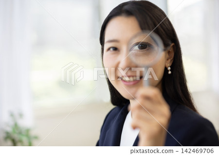 A young Japanese businesswoman holds a magnifying glass towards the camera. A young Japanese businesswoman holds a magnifying glass towards the camera. 142469706