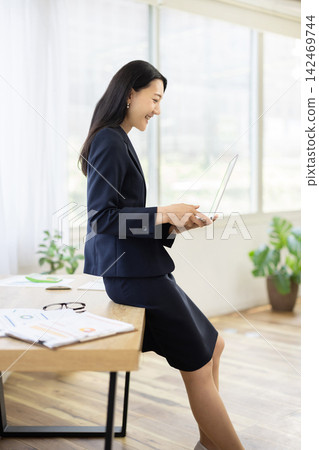 A young Japanese businesswoman is using her laptop at a desk by a bright window. A young Japanese businesswoman is using her laptop at a desk by a bright window. 142469744